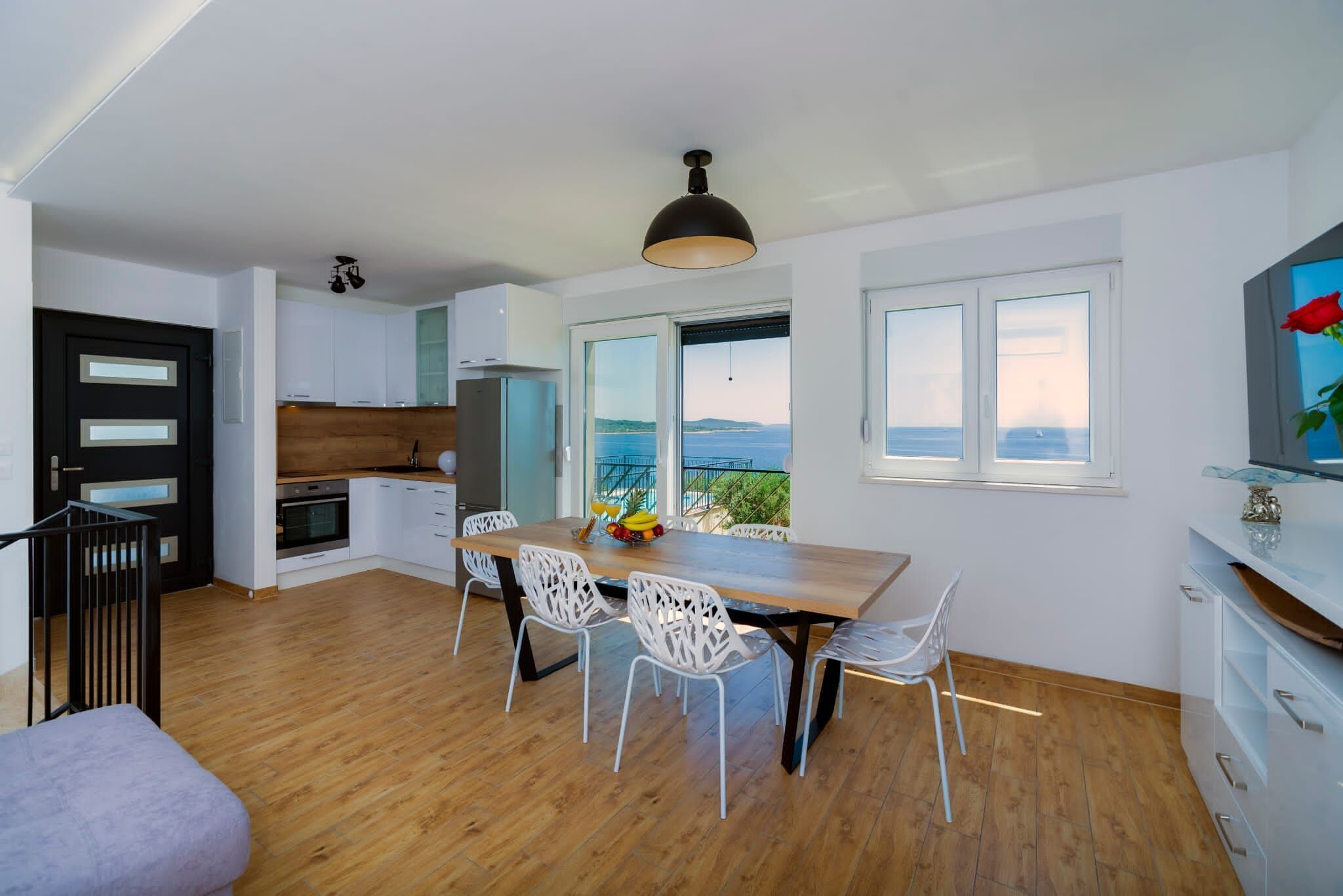 Una cocina moderna con armarios blancos, encimera de madera y un comedor con mesa de madera y sillas blancas.
