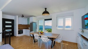 A modern kitchen with white cabinets, a wooden countertop, and a dining area with a wooden table and white chairs. - Villa Adio Mare (Rogoznica)