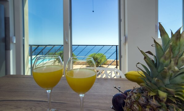 Two glasses of yellow beverage on a wooden table with a banana and pineapple nearby, overlooking a balcony with a view of the sea. - Villa Adio Mare (Rogoznica)