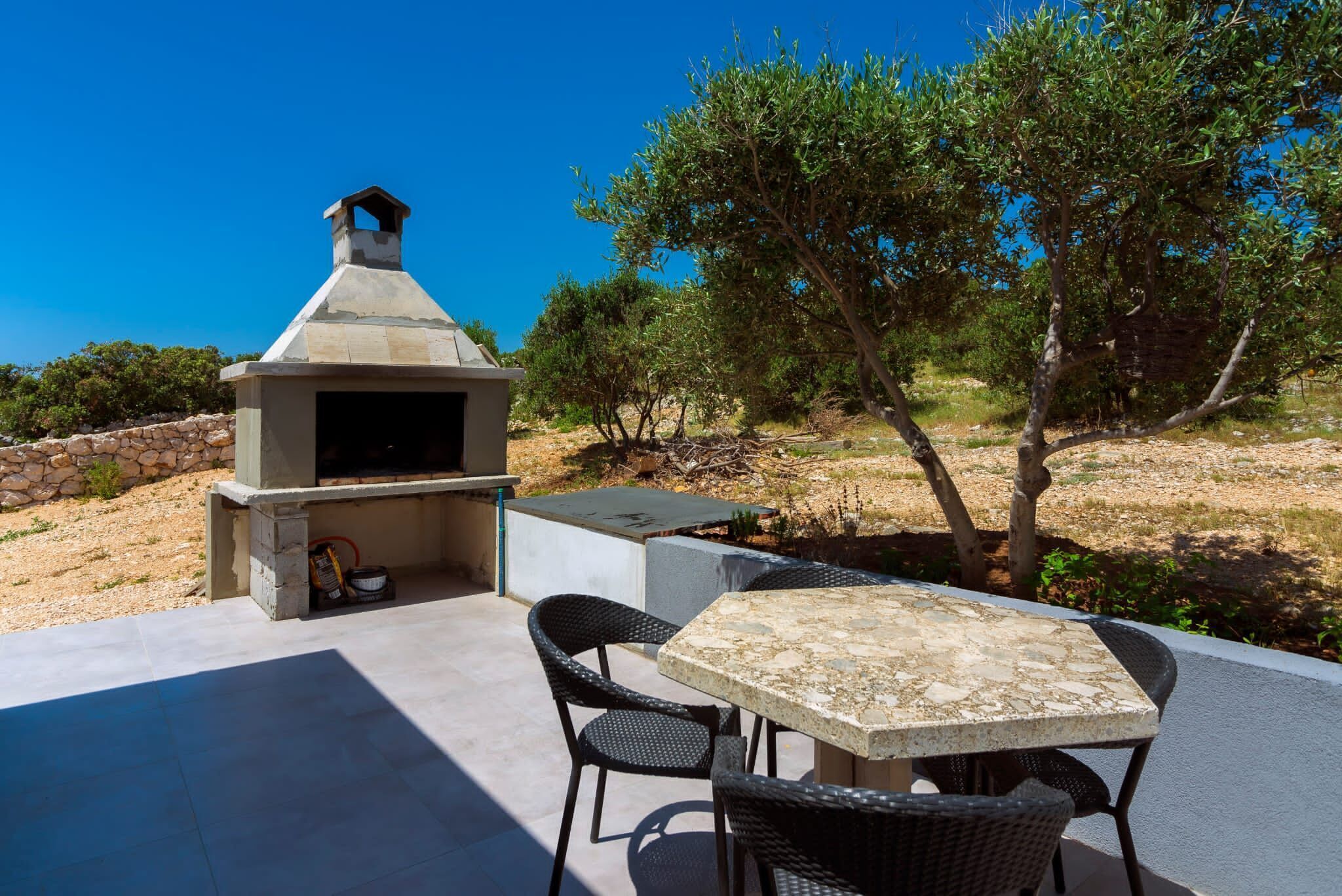 Eine Terrasse im Freien mit einem Steinkohlegrill, einem Tisch und Stühlen.