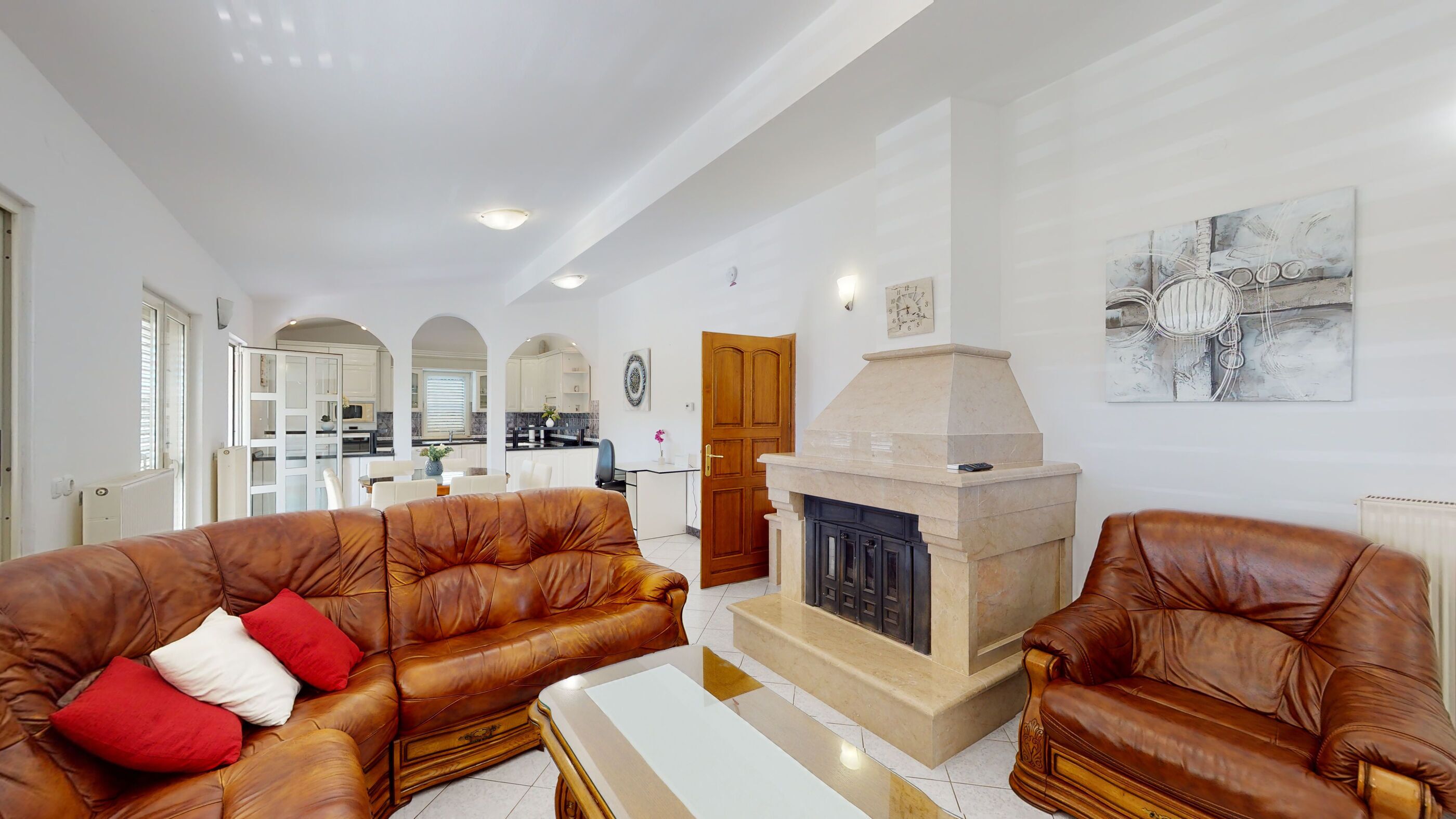 A spacious living room with leather sofas, a fireplace, and a kitchen in the background.