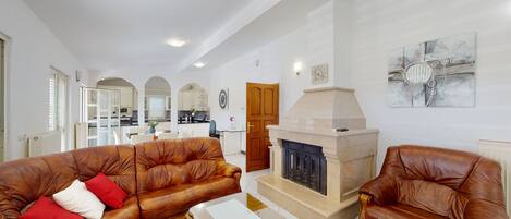 A spacious living room with leather sofas, a fireplace, and a kitchen in the background.