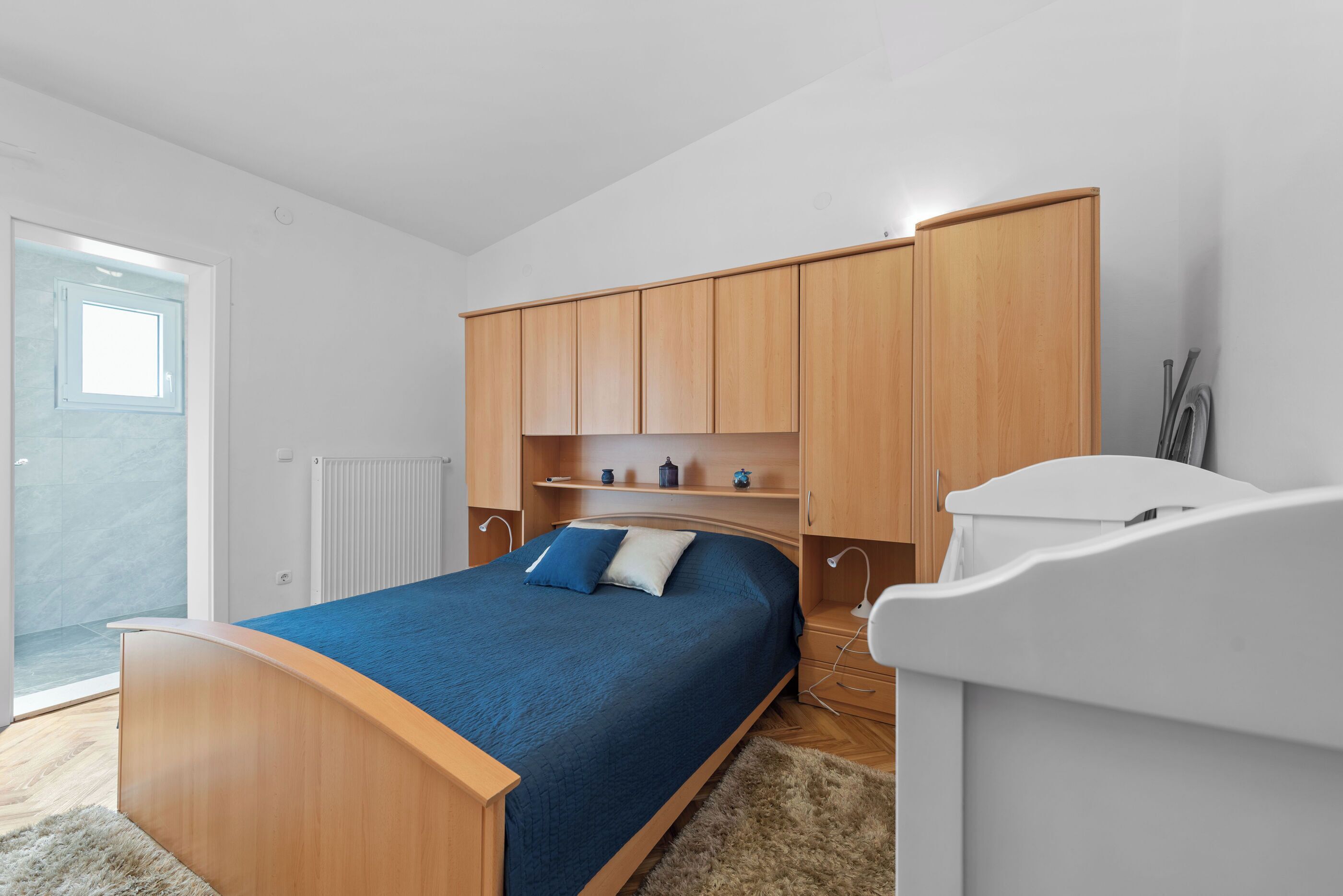 A bedroom with a bed, wooden wardrobe, bedside table, and a white headboard.