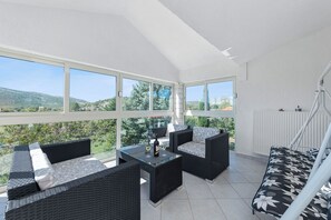 A sunlit patio with wicker furniture, a glass table, and a view of green hills. - Villa Almas (Muc)
