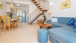A modern living room with a blue sofa, wooden dining table, and a staircase with orange steps. - Villa Holiday Reunion (Pirovac)