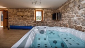 A room with a stone wall, a wooden door, a blue bench, and a hot tub. - Villa Grgo (Rogoznica)