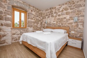 A bedroom with a stone wall, a wooden bed, a nightstand, and a window. - Villa Grgo (Rogoznica)