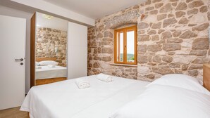 A bedroom with a stone wall, a wooden door, a window, and a bed with white linens. - Villa Grgo (Rogoznica)