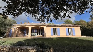 Una casa de dos pisos con un patio, un televisor y una mesa con sillas.