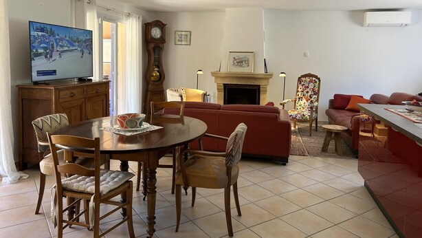 Un salón con una mesa de comedor, sillas, un sofá, una chimenea, un televisor y un reloj.