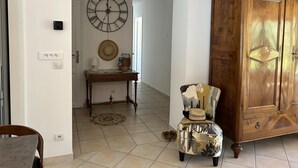 Un pasillo con un armario de madera, un reloj de pared redondo, una mesita con una lámpara y una silla.