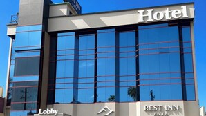 Ein Hotel mit moderner Glasfassade, einem sichtbaren Lobbybereich und der Beschilderung 'REST INN BJAJA'.