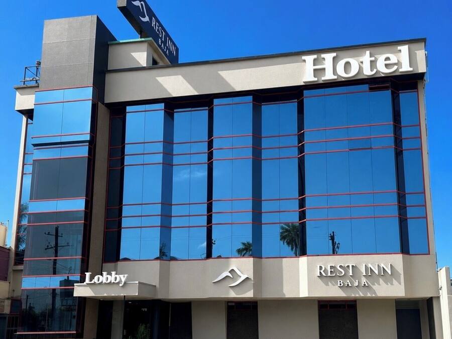 A hotel with a modern glass facade, a visible lobby area, and signage indicating 'REST INN BJAJA.'