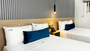 Ein Hotelzimmer mit zwei Betten, jeweils mit weißer Bettwäsche und blauen Kissen, einem Holz-Kopfteil, einer gestreiften Wand und einem Nachttisch mit Telefon.