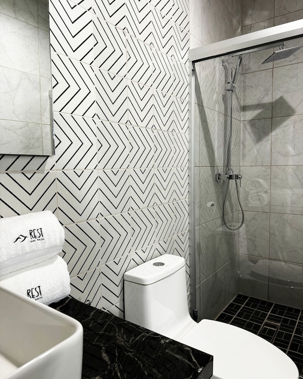 Une salle de bain moderne avec un mur orné d’un motif en chevrons noir et blanc, une douche, des toilettes et un lavabo doté d’un plan de travail en marbre.
