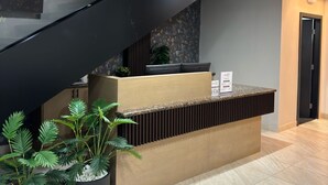 Ein moderner Empfangstresen mit Glastrennwand, eine schwarze Treppe und Kübelpflanzen.
