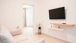 A modern living room with a beige sofa, a flat-screen TV mounted on the wall, and a small wooden shelf below it. - IDEAL HOUSE TO DISCONNECT FROM THE ROUTINE.  SUN, SEA AND RELAXATION. (Las Playitas)