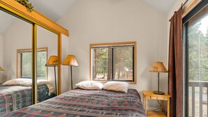Une chambre avec deux lits, un grand miroir, une fenêtre donnant sur les arbres et une lampe sur une table de chevet.