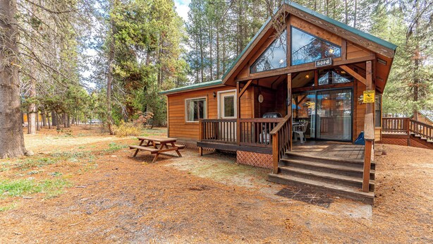Une cabane dotée d’une véranda, d’une table de pique-nique et d’un escalier menant à l’entrée.