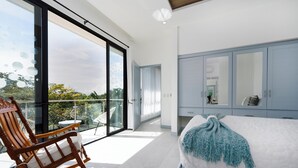 Ein modernes Schlafzimmer mit einem großen Bett, einem Schaukelstuhl und einem Balkon mit Glastür.