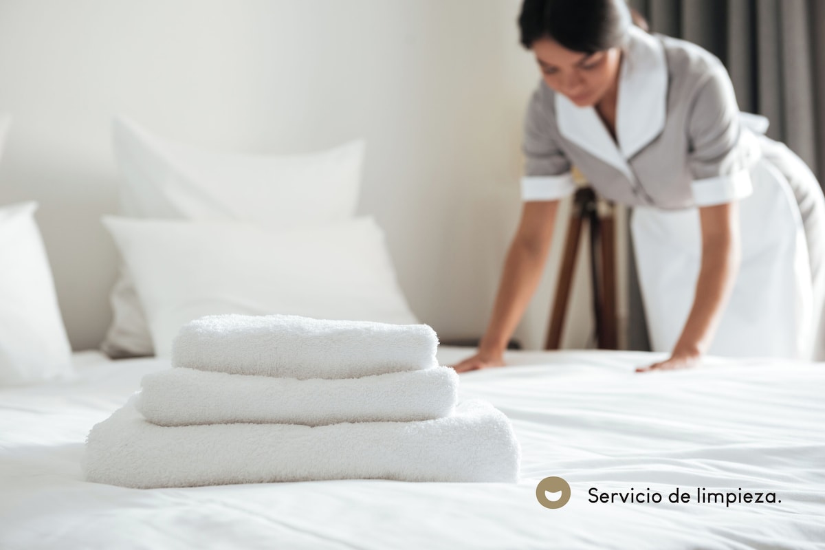 A neatly made bed with folded white towels and a person in a uniform leaning over the bed.