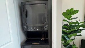 Ett litet och praktiskt tvättrum med en inbyggd tvättmaskin och torktumlare, en krukväxt och en vit dörr.