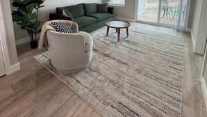 Ett vardagsrum med en grön soffa, en beige fåtölj, ett runt soffbord, en stor matta, en takfläkt och en tavla med ett björnmotiv på väggen.