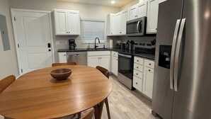 A modern kitchen with white cabinets, a stainless steel refrigerator, a microwave, and a dining table with wooden chairs. - Kapilana - Pelican Unit H- Lakefront w/Boat Rental (Osage Beach)
