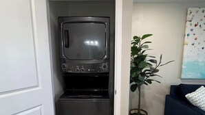 A compact kitchenette with a built-in microwave and refrigerator, a potted plant, and a blue sofa in a modern apartment. - Kapilana Beach Unit I - Lakefront! w/Boat rental (Osage Beach)