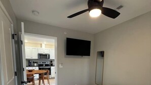 Une chambre à coucher avec un lit, un ventilateur de plafond et un téléviseur fixé au mur.