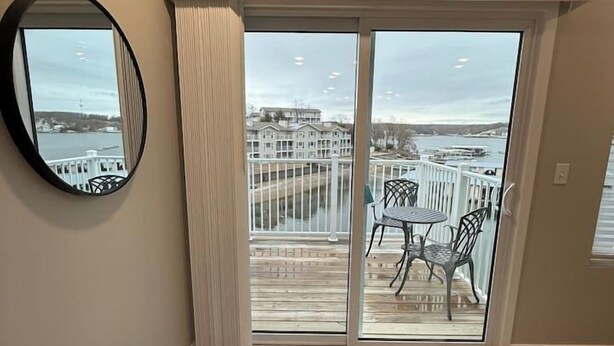 Une pièce spacieuse dotée d’une grande porte-fenêtre coulissante qui donne sur un balcon offrant une vue sur le bord de l’eau et les bâtiments environnants.