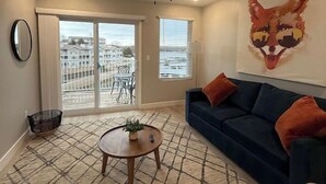 Un salon avec un ventilateur de plafond, un canapé bleu, un tapis à motifs et un grand tableau représentant le visage d’un renard accroché au mur.