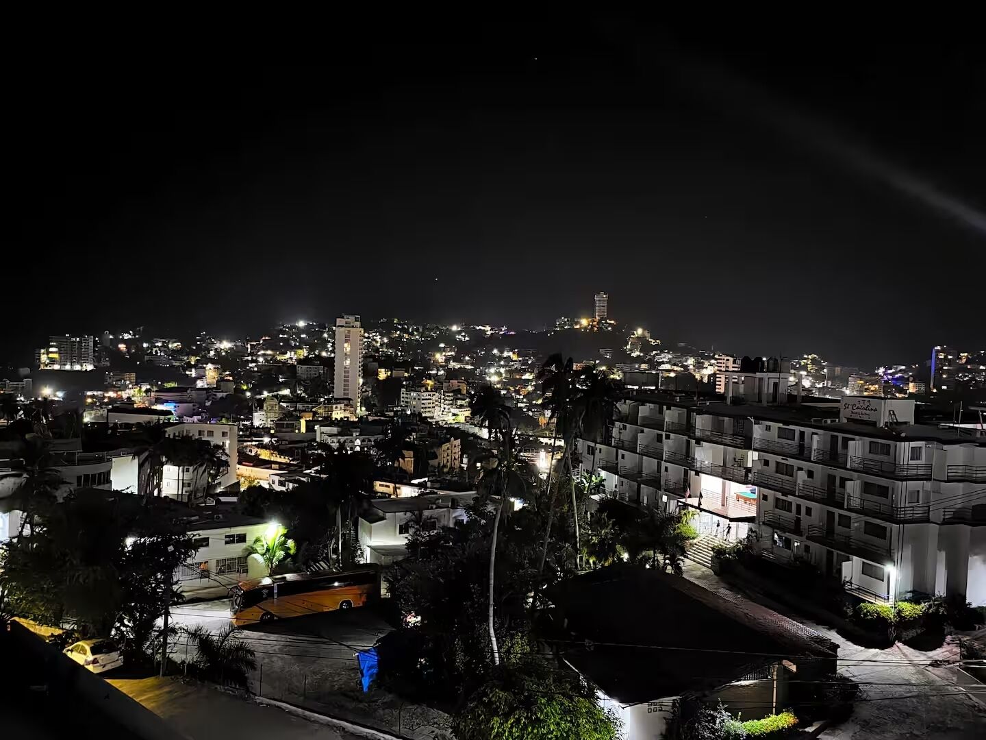 A nighttime cityscape with illuminated buildings and a prominent hilltop structure.