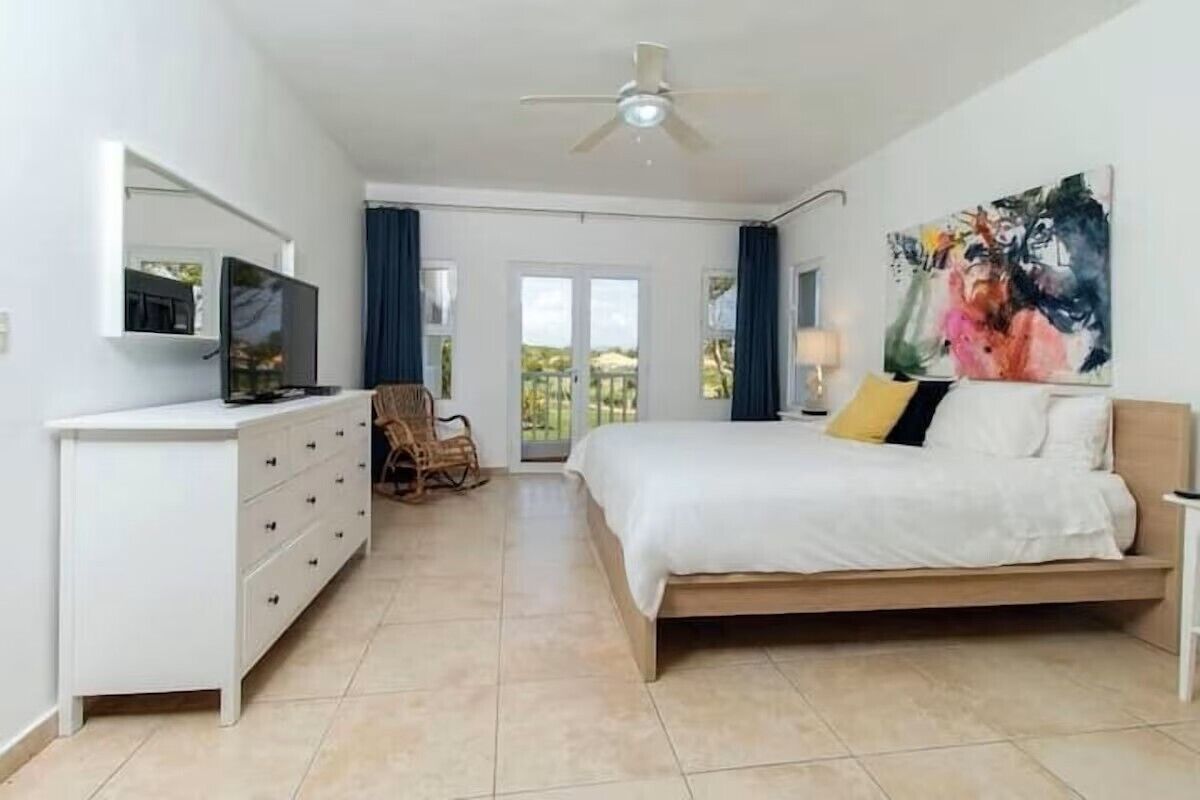 Une chambre à coucher moderne, équipée d’un lit, d’une commode, d’un téléviseur et d’un ventilateur de plafond.
