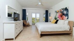 Een moderne slaapkamer met een bed, een dressoir, een televisietoestel en een plafondventilator.