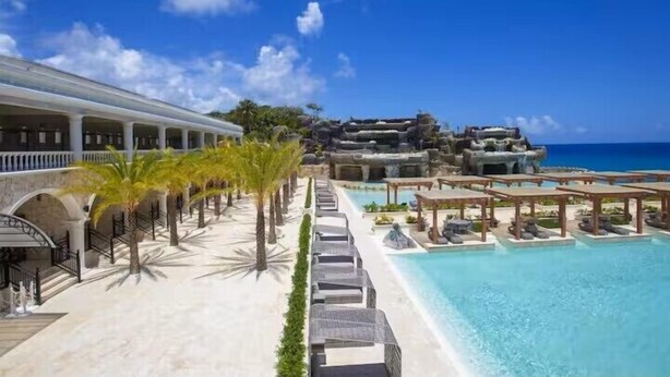 Een resort met een zwembad, palmbomen en uitzicht op zee.