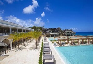 Um resort com piscina, palmeiras e vista para o oceano.