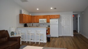 A kitchen with wooden cabinets, a white refrigerator, and a bar area with three white stools.