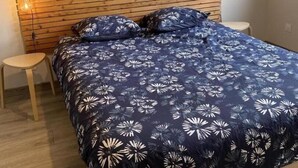 A bedroom with a wooden headboard, a floral-patterned bedspread, a small wooden stool, and two wall-mounted light fixtures.