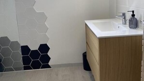 A modern bathroom with a white sink, wooden vanity, and a hexagonal tile backsplash.