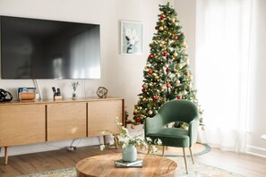 A living room with a wooden TV stand, a green armchair, a round coffee table, and a Christmas tree. - Savannah Retreat | Private Spa | 6 min to Downtown (Savannah)