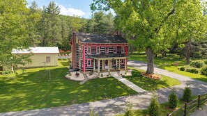 A two-story log cabin with a porch, surrounded by a well-maintained lawn and trees. - Laurel Haven | Private Pool + Fireplace (Rebersburg)