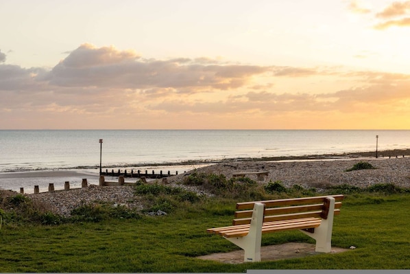 A bench by a beach with a clear view of the sea and a cloudy sky. - Luxury Beachfront Retreat for 14 With Hot Tub (Bognor Regis)