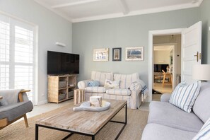A living room with a grey sofa, a wooden coffee table, a TV on a wooden stand, and framed pictures on the wall. - Luxury Beachfront Retreat for 14 With Hot Tub (Bognor Regis)