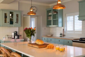 A kitchen with light blue cabinets, a wooden island with bread and juice, and pendant lighting. - Luxury Beachfront Retreat for 14 With Hot Tub (Bognor Regis)