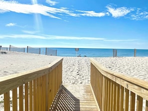 A wooden boardwalk leading to a sandy beach with a clear blue sky and calm sea. - Gulf Village 114 (Gulf Shores)