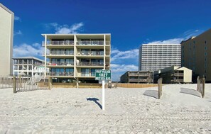 A beachfront hotel with multiple balconies, a sign indicating 'Gulf Village 1027 West Bch. Blvd.', and a sandy beach area. - Gulf Village 114 (Gulf Shores)