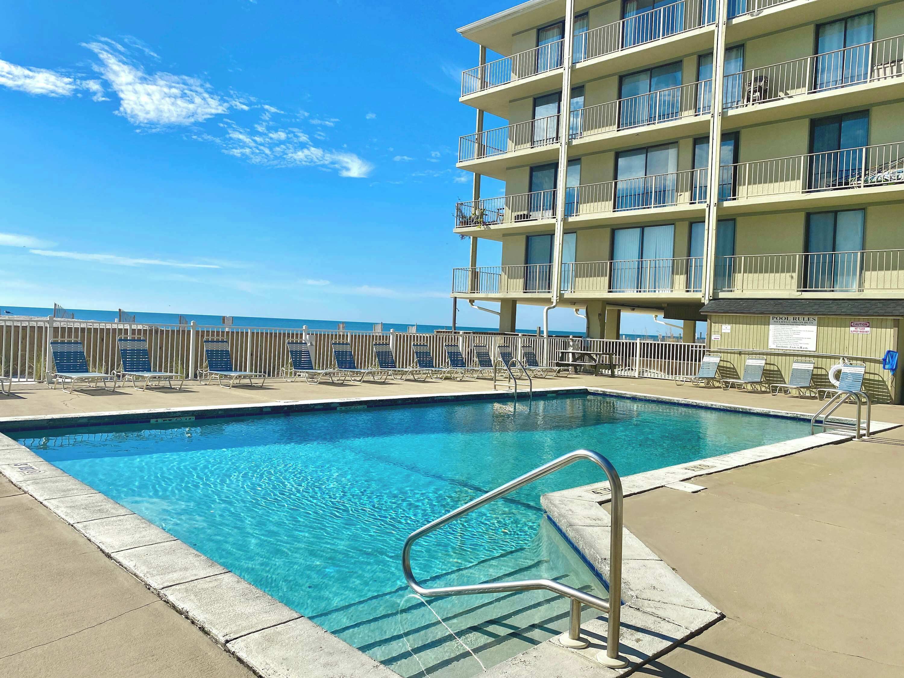 A pool area with clear blue water, a metal pool ladder, and lounge chairs.