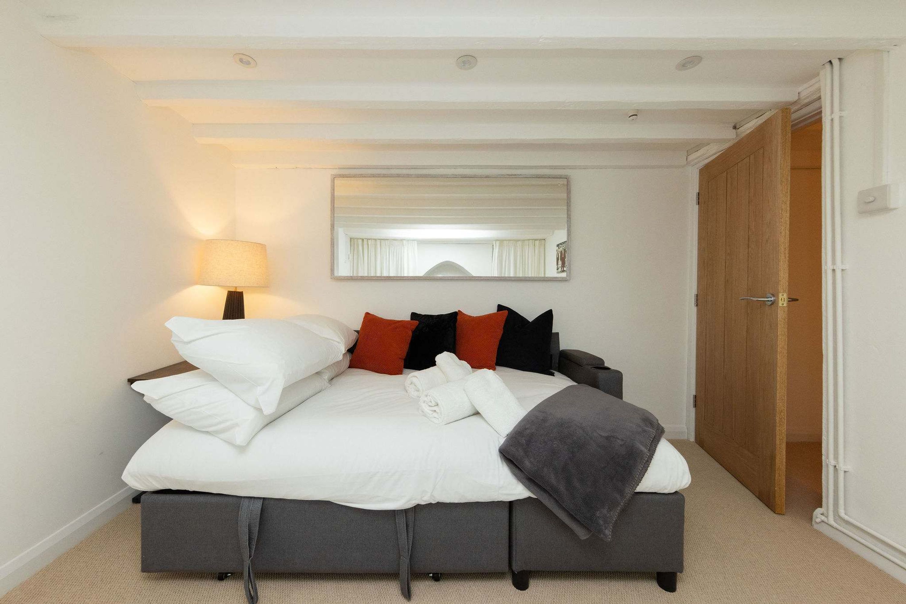 A neatly made bed with white linens, a grey blanket, and a grey pillow.