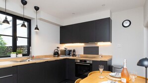 Une cuisine moderne avec des meubles de couleur sombre, un plan de travail en bois et un coin repas avec une table dressée pour deux personnes.